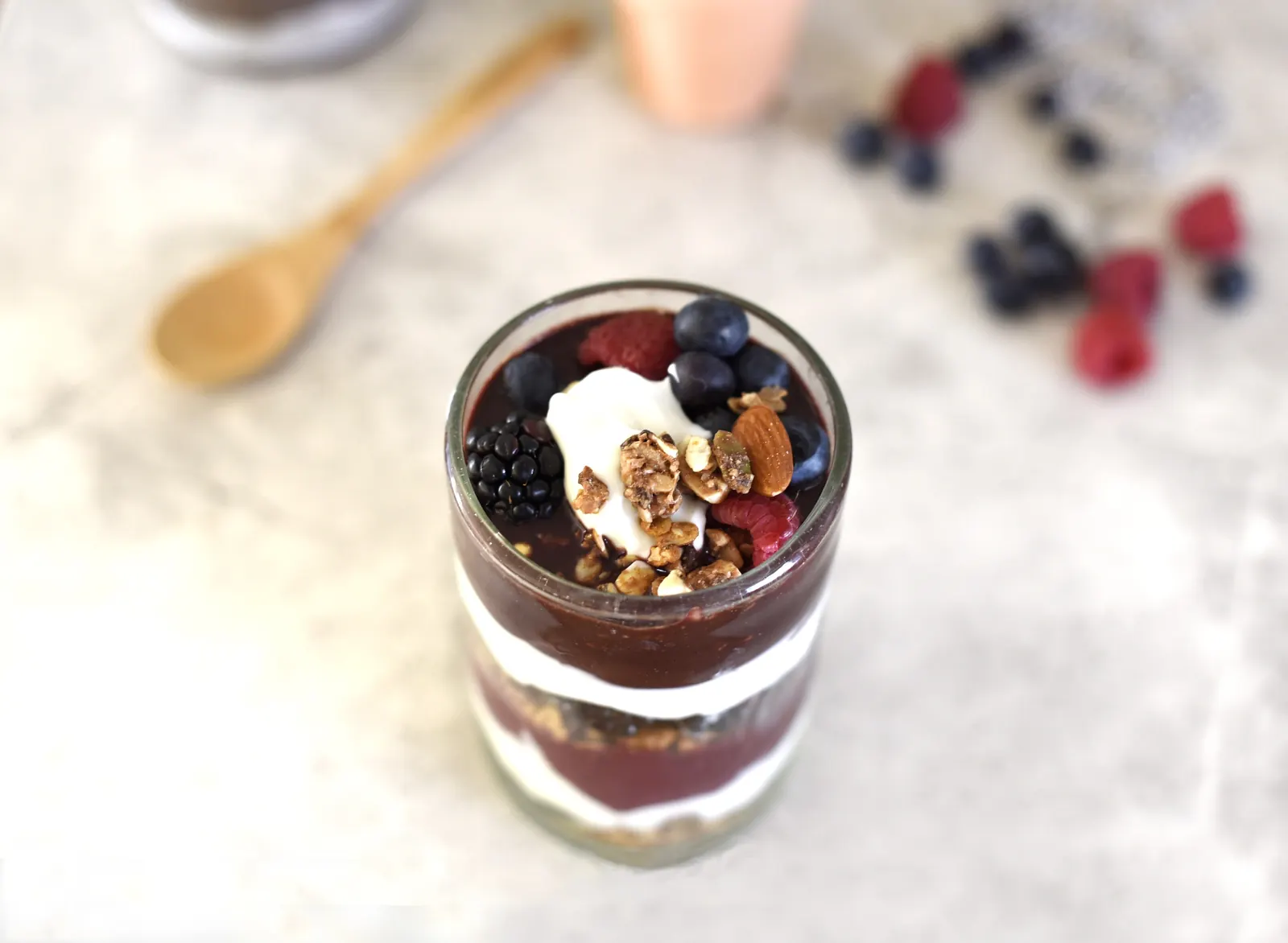 Copo de iogurte com frutas vermelhas, granola e amêndoas sobre a mesa.