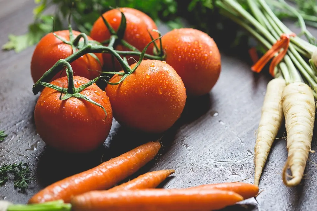 Tomates e cenouras frescos sobre uma bancada escura.